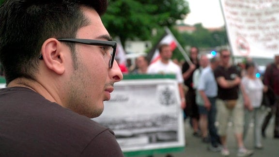 Ein Mann mit Brille steht neben einer Demonstration.