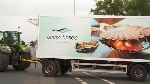 Ein Traktor zieht einen Anhänger mit der Aufschrift ’deutschesee’.