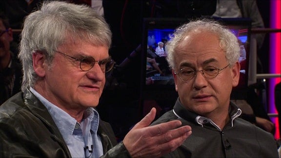 Zwei Männer mit Brille sitzen in einer Talkrunde.