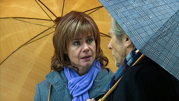 Eine Frau und ein Mann unter Regenschirmen im Gespräch.
