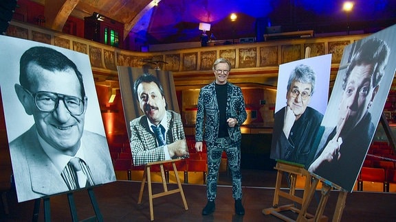 Ein Mann steht im Zentrum von vier großen Männerporträts, die auf einer Bühne aufgestellt wurden.