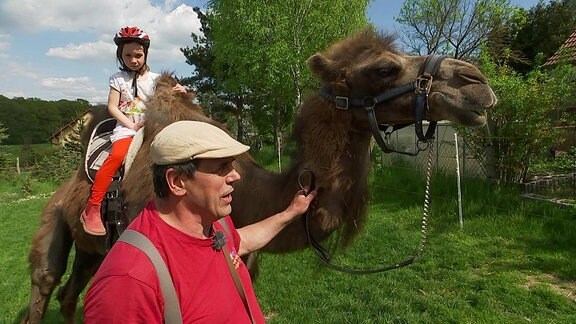 Ein Mann führt ein Kamel, auf dem ein Kind reitet.