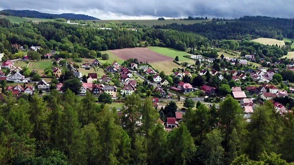 Blick auf die bunten Häuser eines Dorfes, umgeben von Wiesen, Feldern und Wald.