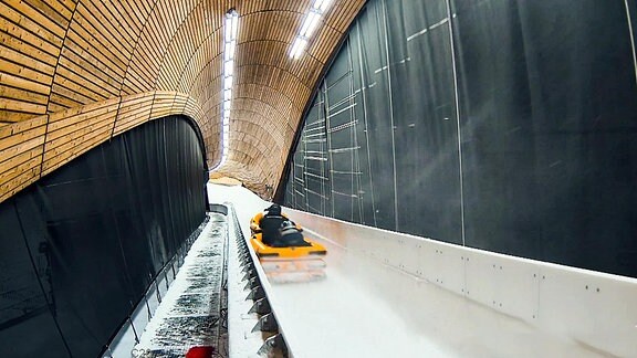 Blick in den Tunnel einer Rodelbahn, in der ein gelber Luftkissenschlitten fährt.