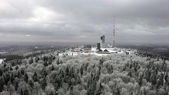 Blick auf einen winterlich bewaldeten Berg, auf dem ein Turm und weitere Gebäude stehen.