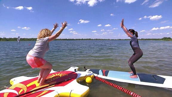 Zwei Frauen auf im Wasser liegenden Boards machen Jogaübungen.