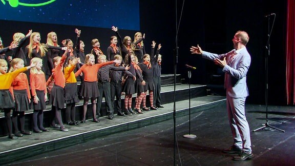 Auftritt Kinderchor mit Chorleiter (Kinder reißen die Arme hoch)