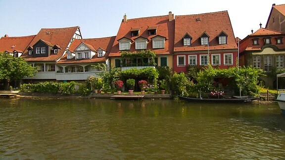Blick auf eine blühende Häuserreihe, die dicht an ein Gewässer gebaut ist.
