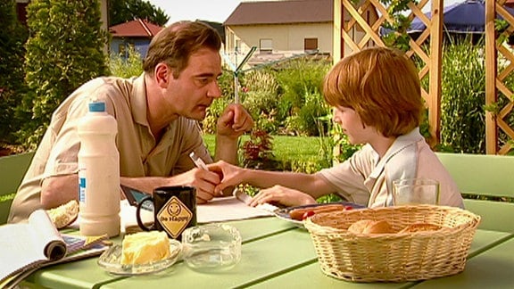 Mann unterschreibt einen Brief mit Kind an einem Gartentisch