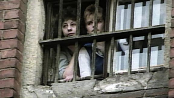 Zwei Frauen stehen an einem vergitterten Fenster