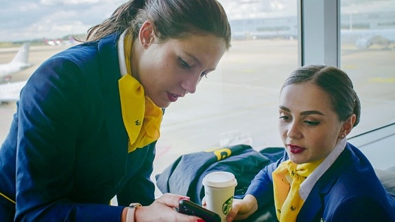 zwei Stewardessen in Uniform schauen in ein Funktelefon
