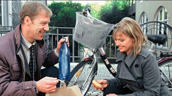 Pauske (Oliver Stritzel) hilft Karin (Katharina Böhm) dabei, herausgefallene Einkäufe wieder in die Einkaufstüten zu sammeln. Beide knien und lächeln sich an, Pauske fühlt sich sichtlich zu Karin hingezogen.