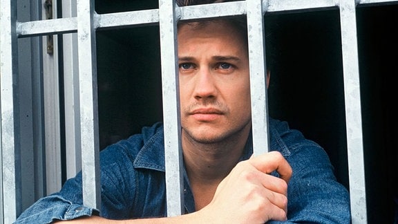 Andreas (Kristian Kiehling) steht an seinem vergitterten Gefängnisfenster und blickt sehnsüchtig hinaus.