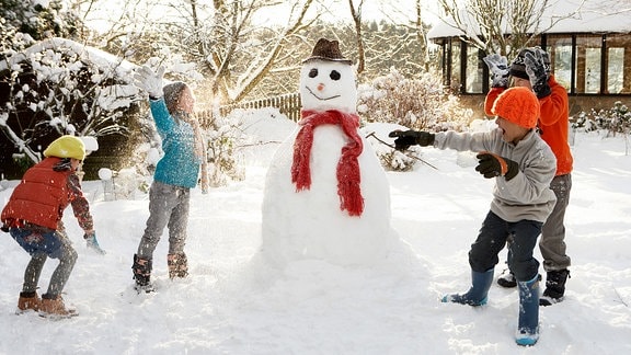Kinder spielen um einen Schneemann herum.