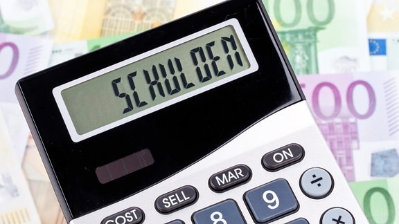 Das Wort "Schulden" steht auf einem Taschenrechner, der auf Euro-Banknoten liegt