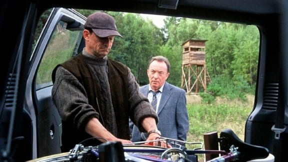 Karsten Dietz (Thomas Sarbacher, l.) nimmt Hauptkommissar Ehrlicher (Peter Sodann, r.) mit zum Luderplatz und verstaut dafür Ehrlichers Fahrrad in seinem Jeep.