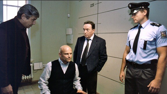 Jochen Krause (Alexander Radszun, Mitte) beteuert seine Unschuld. Kommissar Ehrlicher (Peter Sodann, 2.v.r.) und Major Cerny (Zdenek Maryska, links mit Lubos Pecenka, rechts) zweifeln an seinen Aussagen.