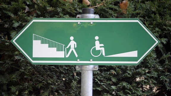 Ein Schild weist darauf hin, dass Fußgänger links eine Treppe und Rollstuhlfahrer rechts eine Auffahrt benutzen können