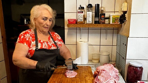 Eine Frau steht in einer Küche und schneidet Fleisch