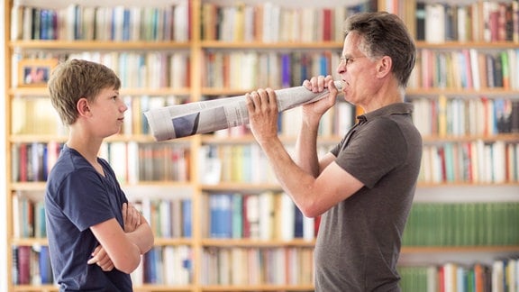 Vater schreit durch ein Megafon aus Zeitungspapier seinen Sohn an.