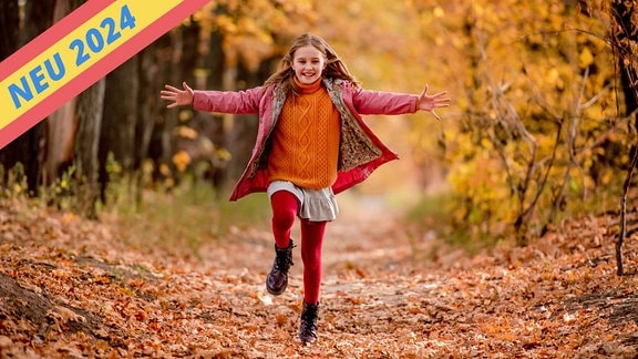 Ein Mädchen läuft mit ausgebreiteten Armen durch eine Herbstlandschaft.