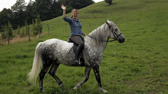 eine Frau sitzt auf einem Pferd und winkt 