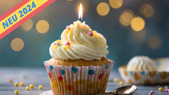 A beautifully decorated cupcake with white frosting and a lit candle, sitting on a wooden surface with a bokeh background, capturing a festive celebration moment