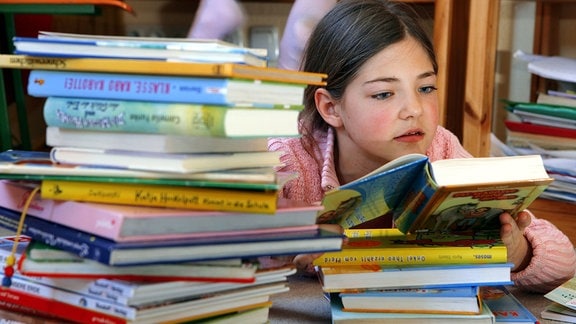 Ein Kind liest ein Buch, daneben hohe Bücherstapel.