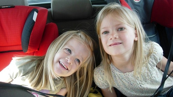Zwei kleine Mädchen auf ihren Autokindersitzen.
