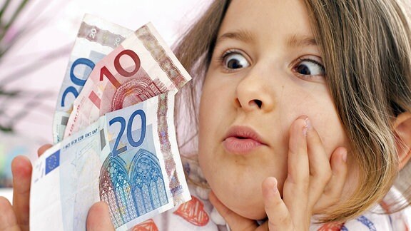 Ein Mädchen schaut erstaunt auf Geldscheine, die es in seiner Hand hält