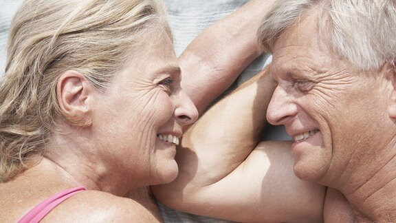 Ein älteres Paar liegt vertraut nebeneinander draußen auf einer Decke. 