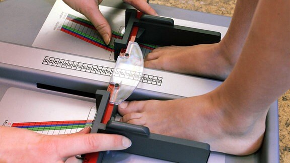 Nackte Kinderfüße werden mit einem Fußmessgerät vermessen