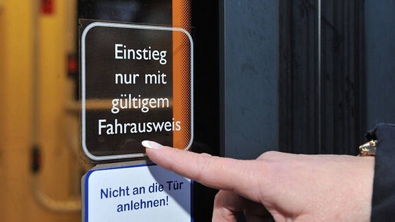 Eine Frau zeigt auf einen Hinweisaufkleber am Fenster einer Straßenbahn mit der Aufschrift Einstieg nur mit gültigem Fahrausweis.