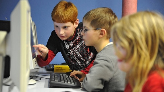 Etwa zwölf Jahre alte Kinder sitzen vor Computern.