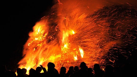 Bei Nacht stehen Menschen gemeinsam vor einem Osterfeuer.