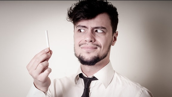 Geschäftmann blickt mit verzerrtem Gesicht auf Zigarette in seiner Hand
