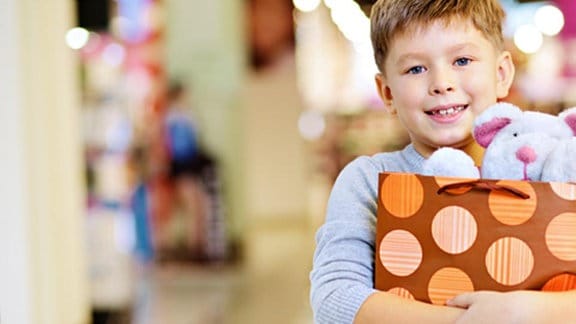 Ein Junge hält stolz eine Einkaufstüte mit einem Teddybären darin.