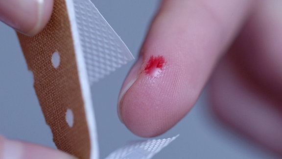 Eine junge Frau blutet am Finger wird mit Pflaster verarztet.