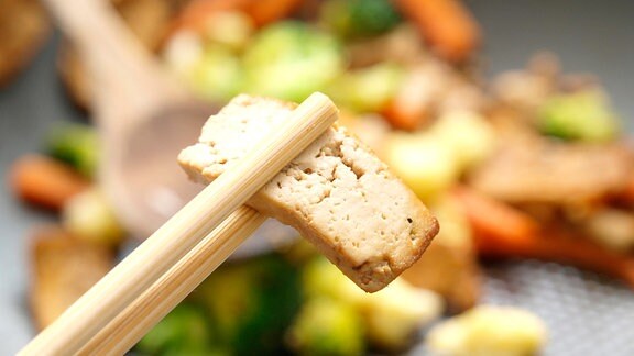 Zwischen zwei Essstäbchen steckt ein Stück Tofu
