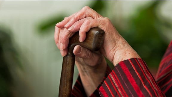 Die Hände einer alten Frau umfassen den Griff eines Gehstocks.
