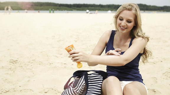 Eine Frau reibt sich mit Sonnencreme am Strand ein.
