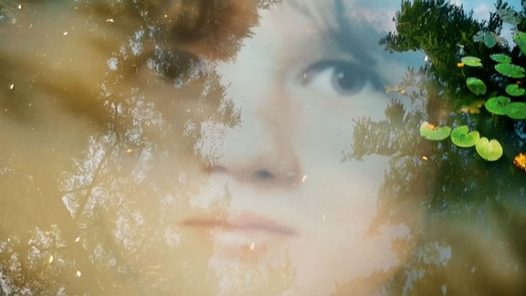 Das Gesicht eines jungen Mädchens auf der spiegelnden Oberfläche eines Teiches mit Seerosen.
