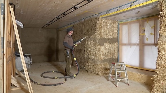 Handwerker bearbeitet eine Wand aus Stroh.