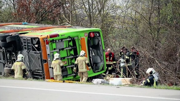 Busunglück; umgestürzter Flixbus neben der Autobahn, Rettungskräfte im Einsatz.