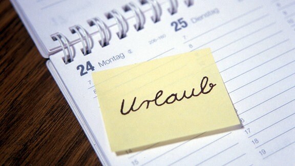 Auf einem Kalender klebt ein Zettel mit der Aufschrift "Urlaub". 