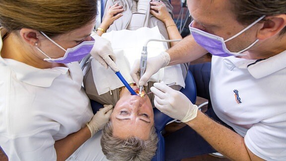 Ein Zahnarzt behandelt mit einer Zahnarzthelferin eine Frau.