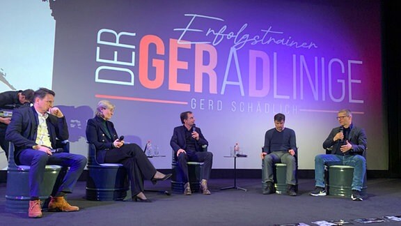 Vier Männer und eine Frauen sitzen auf einer Bühne. Im Hintergrund steht auf einer Leinwand "Der Geradlinige".