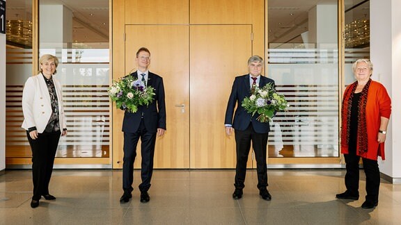 Zwei Männer mit Blumensträußen stehen zwischen zwei Frauen.