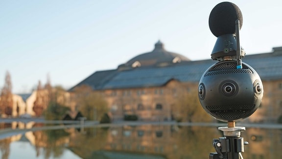 360-Grad-Kamera steht vor einem Teich, in dem sich ein Gebäude spiegelt