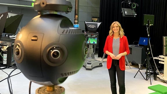 Eine blonde Frau in rotem Sakko lächelt in eine 360-Grad-Kamera 